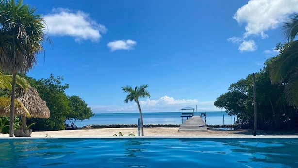 A clear blue pool with a wooden deck leading to a beach. - Gold Standard: Private Home, Infinity Pool on the Beach & Reef View (San Pedro Town)