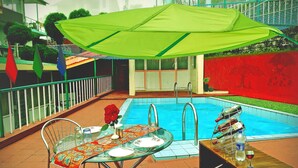 A poolside area with a table set for dining, a pool, and a green umbrella.