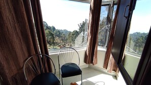 A balcony with two chairs and a table, overlooking a forested area.