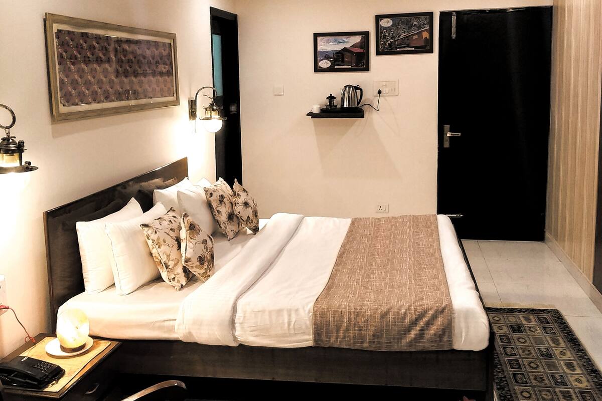 A bedroom with a bed, bedside table, lamp, chair, and a small table with a vase.