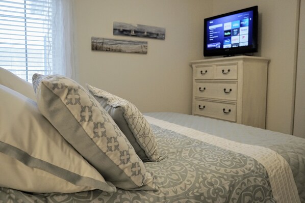 A neatly made bed with patterned bedding, a television on a stand, and a dresser with drawers.