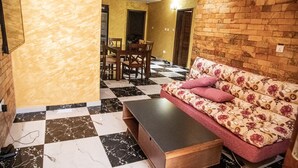 Una habitación con suelo a cuadros, un sofá con tapicería floral, una mesa de centro de madera y una zona de comedor con sillas y una mesa.