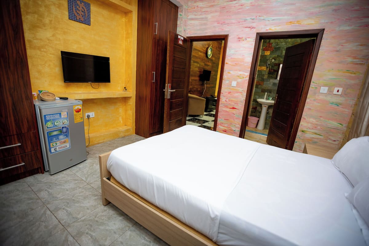 Une chambre à coucher avec un lit, une télévision, un réfrigérateur et une salle de bain visible à travers une porte ouverte.