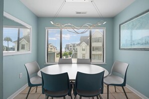 A dining room with a round table and chairs, large windows with blinds, and a ceiling light fixture.