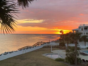 A beachfront property with a pool, a white fence, and a sunset view.