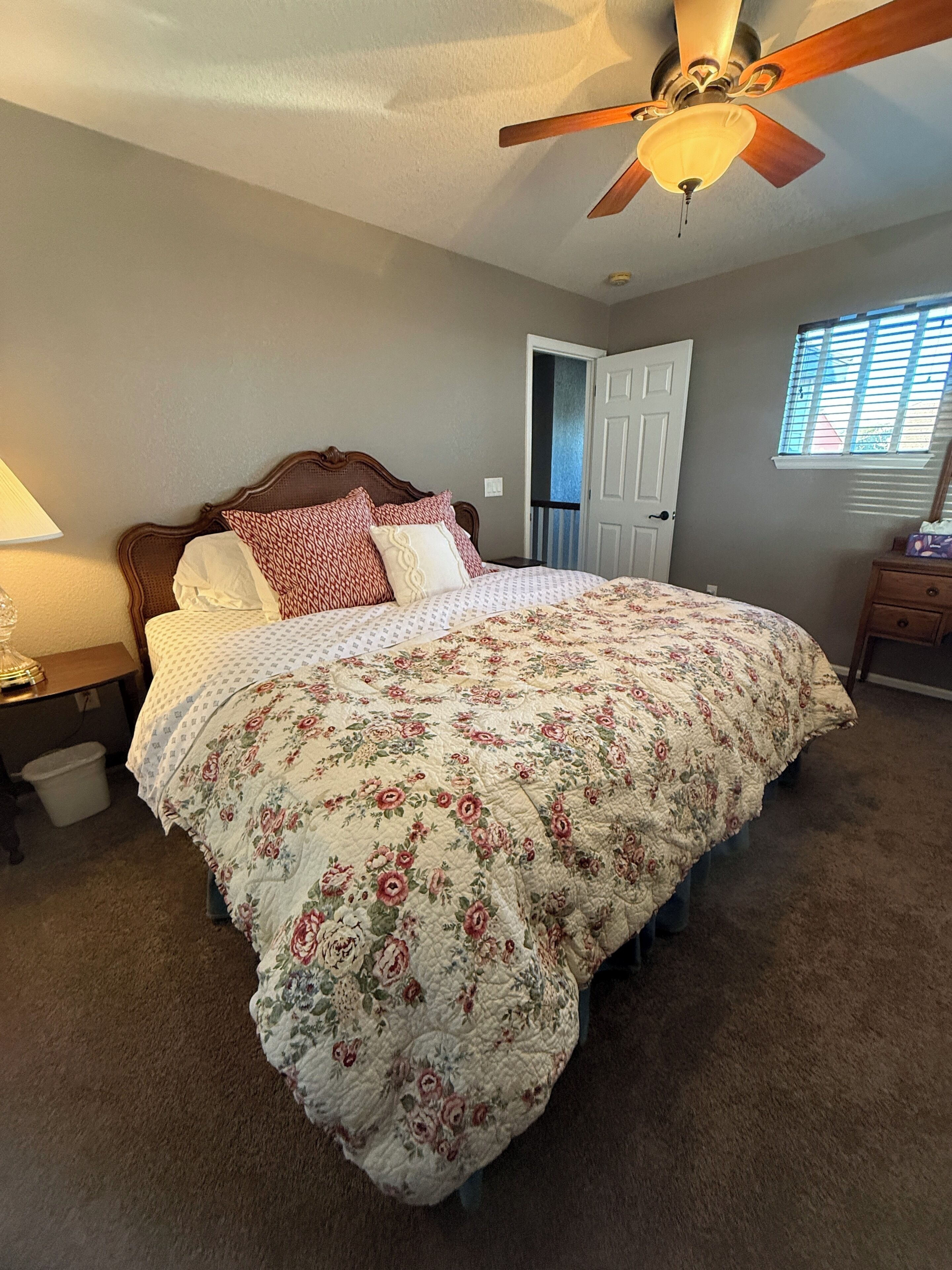 A bedroom with a bed, a ceiling fan, a nightstand, a lamp, a door, and a window.