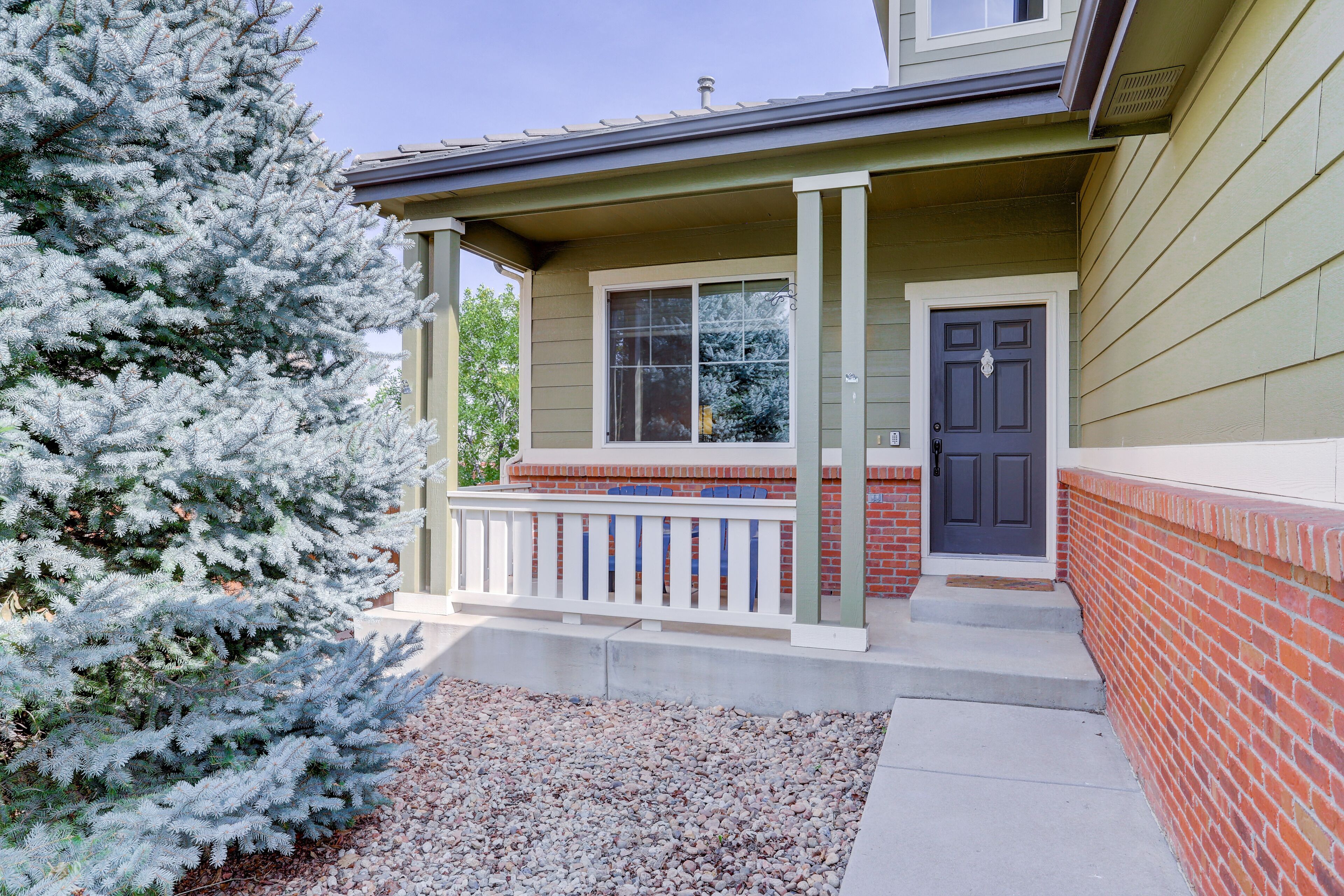 A house with a porch, a front door, and a large evergreen tree.