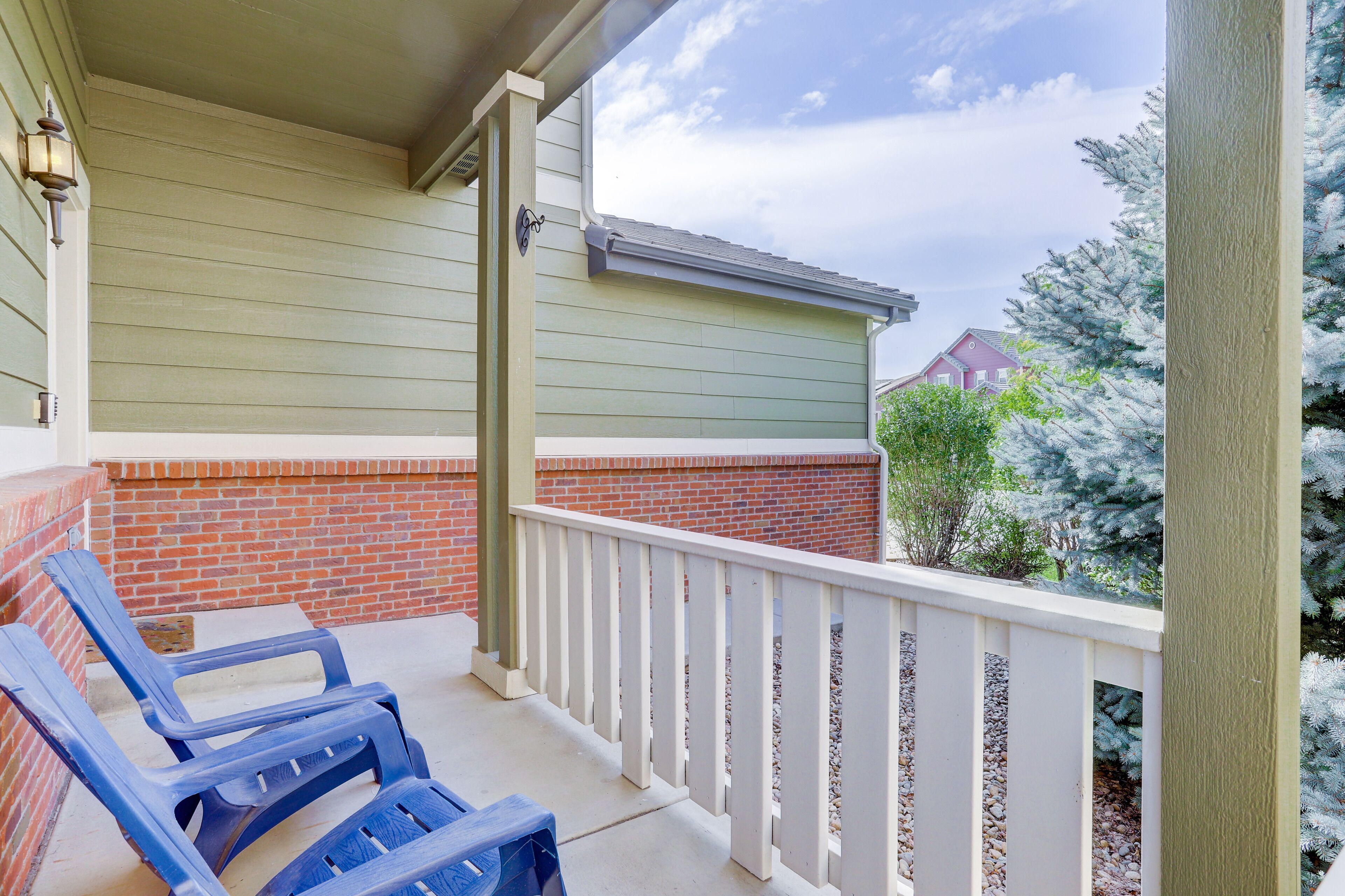 A covered porch with two blue plastic chairs and a white railing.