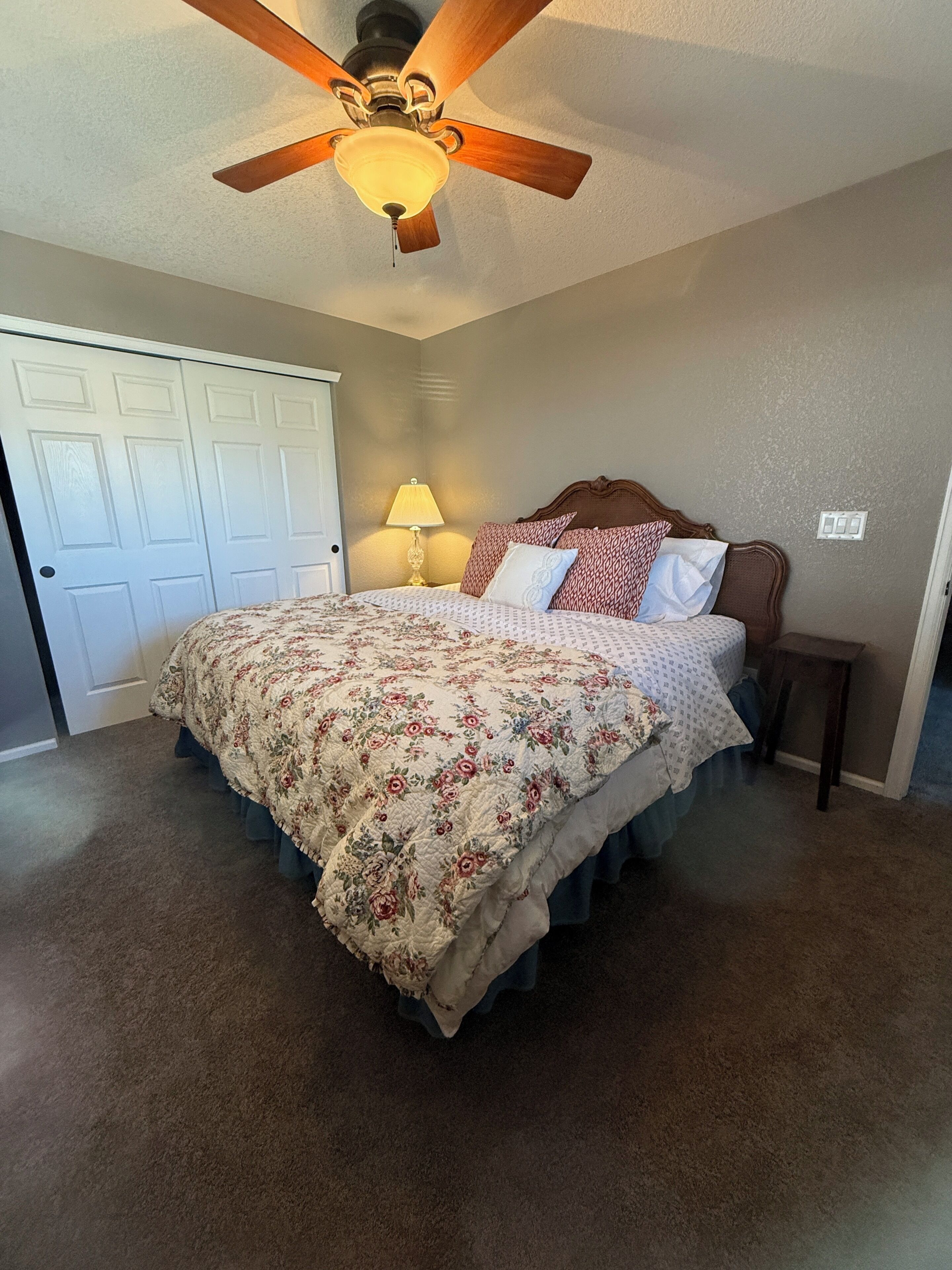 A bedroom with a bed, a ceiling fan, a nightstand, and a lamp.