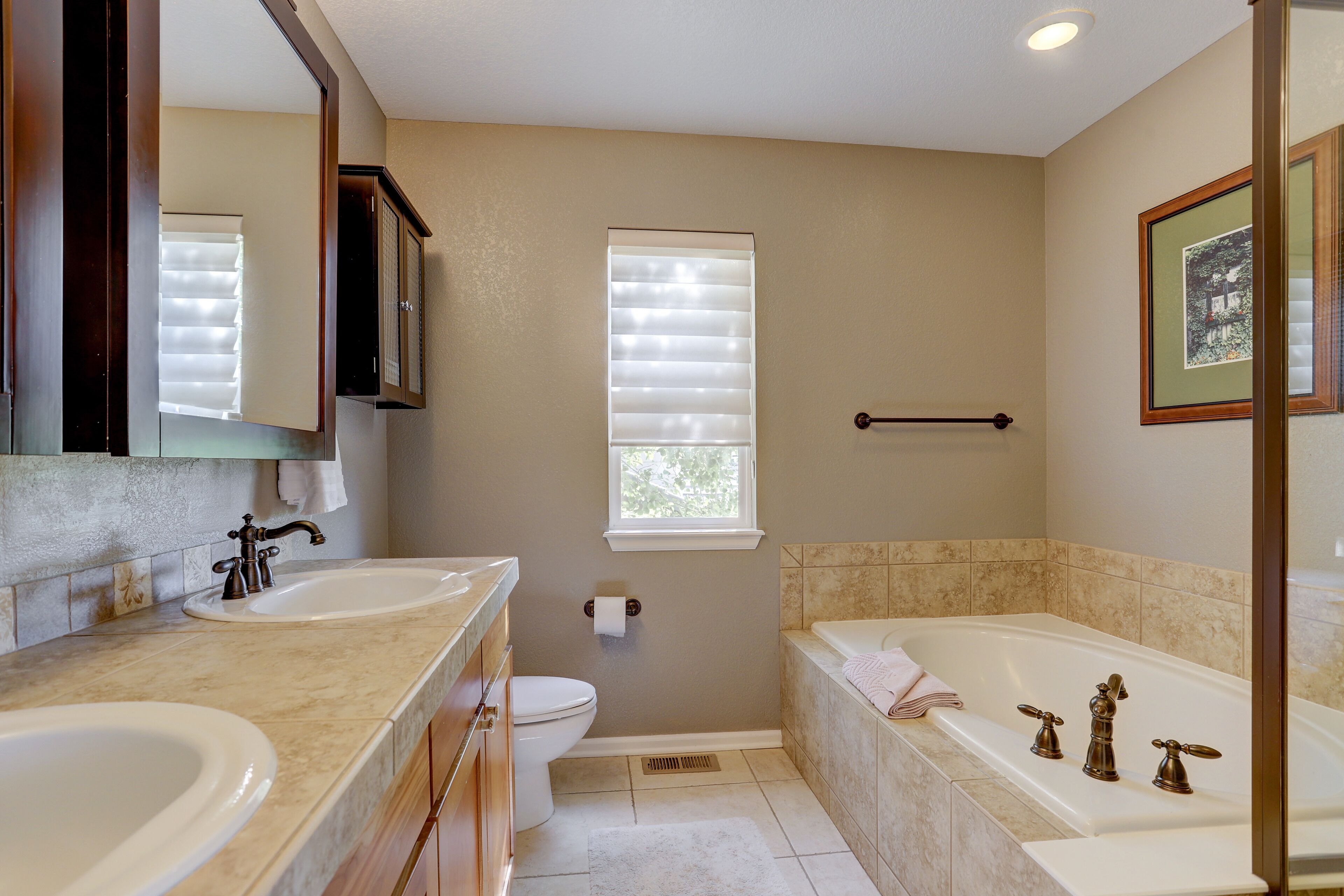 A bathroom with two sinks, a toilet, a bathtub, and a window with blinds.