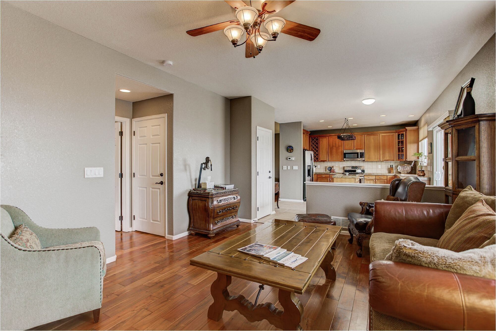 A spacious living room with a wooden coffee table, leather sofa, and a dining area with a chandelier.