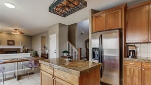 A kitchen with wooden cabinets, a stainless steel refrigerator, a marble countertop, and a ceiling light fixture. - Colorado Greenbelt Vacation Home (Erie)