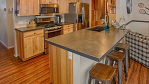 A modern kitchen with wooden cabinets, stainless steel appliances, a central island with stools, and a cozy seating area. - Perfect Pinetop Getaway; 2 Master Suites; Wifi, Satellite; Hot tub, Dog Friendly (Pinetop)