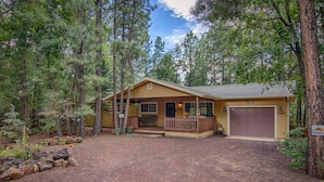 A lodge with a porch, a covered deck, and a garage, surrounded by dense forest. - Perfect Pinetop Getaway; 2 Master Suites; Wifi, Satellite; Hot tub, Dog Friendly (Pinetop)