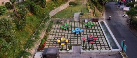Un espacio al aire libre con mesas y sillas, un camino pavimentado y un vehículo estacionado cerca.