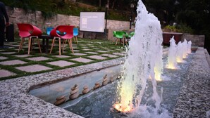 Un élément décoratif aquatique doté de plusieurs jets, un espace de repos avec des chaises et un canal d’eau bordé de pierres.