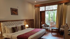 Une chambre d’hôtel avec un grand lit, une tête de lit en bois, une table de chevet, une lampe, une chaise, une table et une fenêtre avec des rideaux.