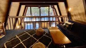 A cozy room with a wooden ceiling, a large window, a wooden bench, a sofa, and a patterned rug. - Cozy family friendly cabin  (Truckee)