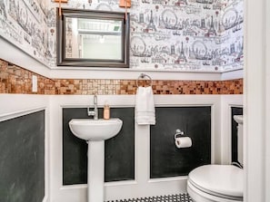 A bathroom with a white sink, a toilet, and a mirror. The walls are decorated with a cityscape wallpaper.