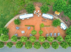 Vista aérea de un camping con dos vehículos recreativos, mesas de picnic y una parrilla.