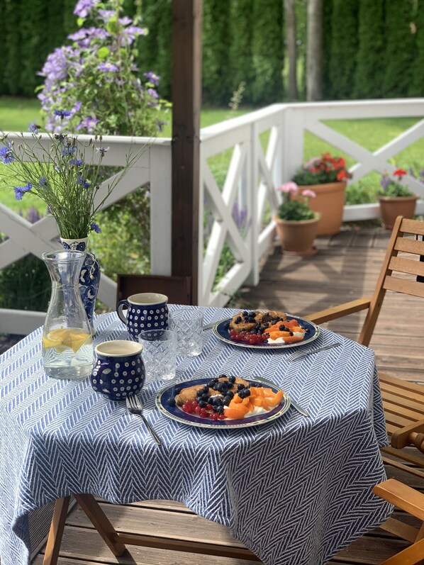 A table set outdoors with a blue and white patterned tablecloth, plates of food, and a vase with flowers.