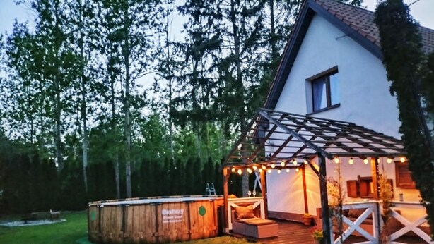 A house with a wooden deck, a pergola with string lights, and a small outdoor seating area.