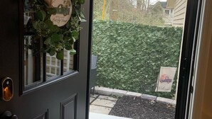 Une porte en bois sombre ornée d’une guirlande, surmontée d’un paillasson et agrémentée d’une élégante heurtoire en métal.