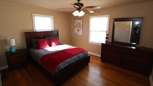 A bedroom with a bed, nightstand, dresser, ceiling fan, and two windows. - Right across street from Expo Center, Fenced Yard (Tulsa)