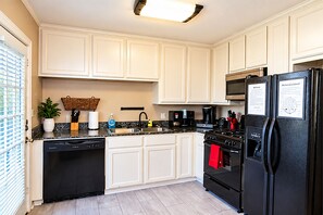 Una cocina con armarios blancos, un lavavajillas negro, un refrigerador negro, un microondas y una estufa.