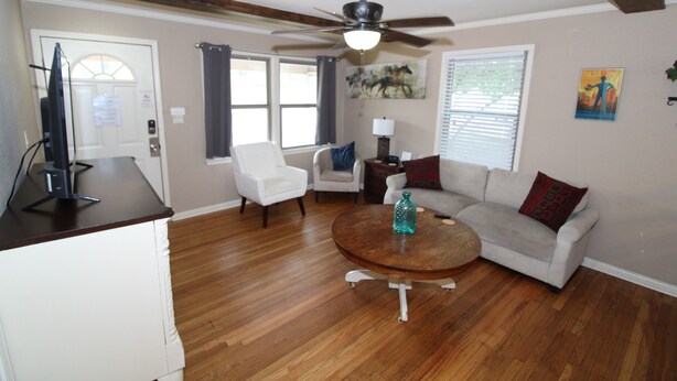 A living room with a ceiling fan, a round coffee table, a sofa, and a TV on a stand. - Right across street from Expo Center, Fenced Yard (Tulsa)