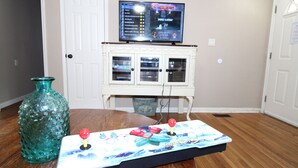 A room with a wooden floor, a white cabinet with glass doors, a television on top, and a game controller on a table. - Right across street from Expo Center, Fenced Yard (Tulsa)