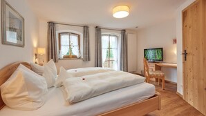 A bedroom with a bed, a desk, a television, and a door. - (06) Comfort vacation apartment with south-east-facing balcony, approx. 67 sqm (Reit im Winkl)