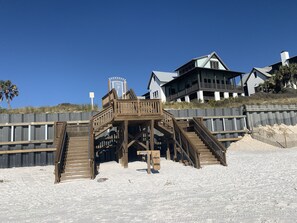 Enjoy the expansive deck with multiple staircases leading to a covered area, offering stunning views of the surrounding beach and ocean.