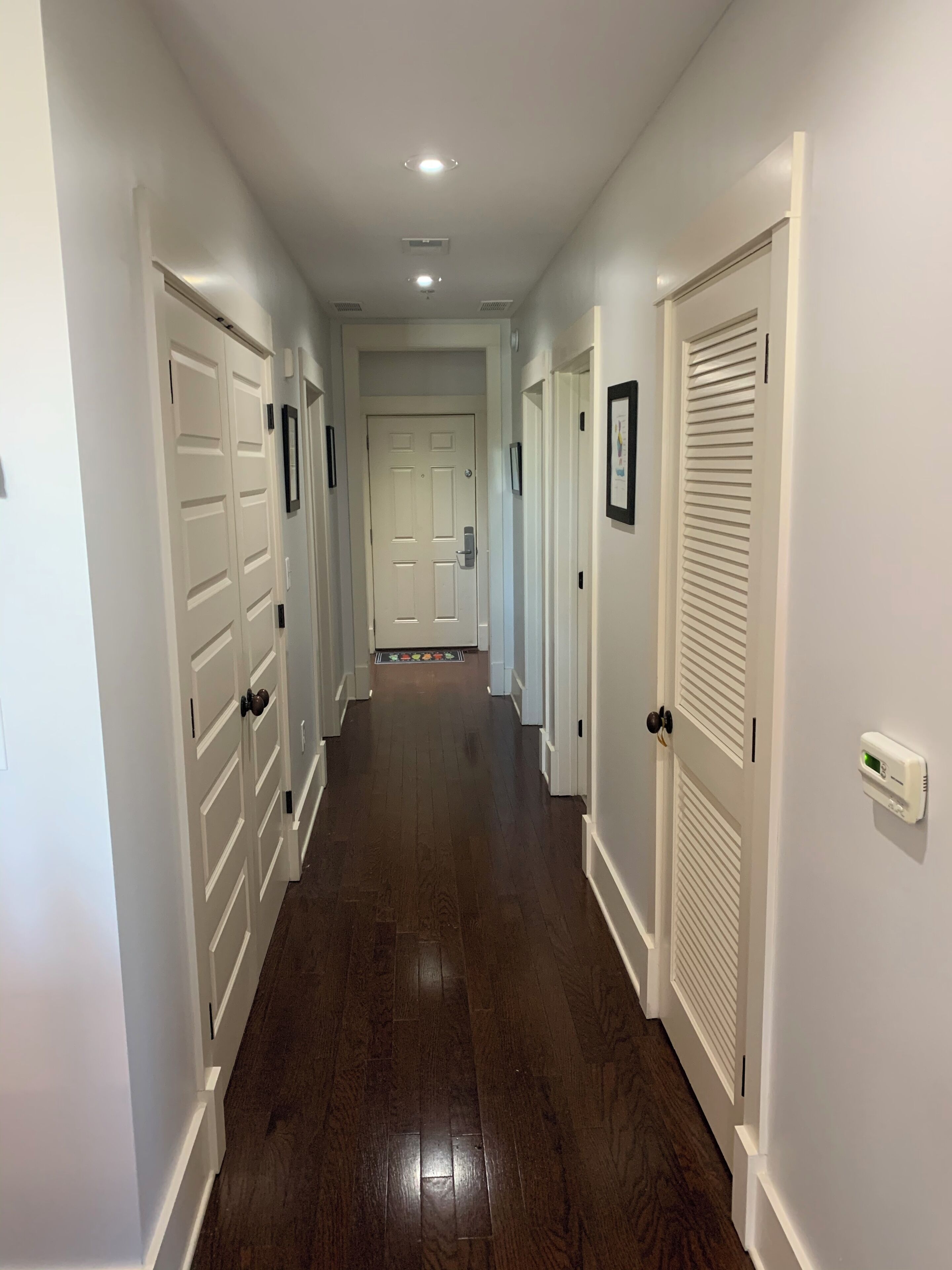A long, narrow hallway with white doors on both sides, leading to a room at the end.