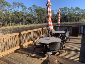 Relax on the deck overlooking the serene water, surrounded by comfortable seating and shaded by striped umbrellas.