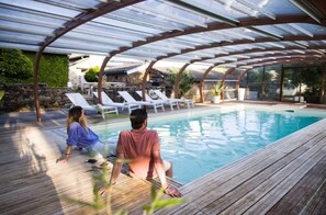 A pool area with a wooden deck, lounge chairs, and a glass-enclosed pergola. - the houses of Salvignol (Martrin)