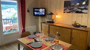 A dining area with a table set for two, a television mounted on the wall, and a scenic painting above the counter. - Cauterets beautifull duplex apartment with terrace (Cauterets)