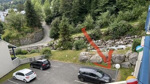 A parking area with several cars, a stone wall, and a view of a forested hillside. - Cauterets beautifull duplex apartment with terrace (Cauterets)