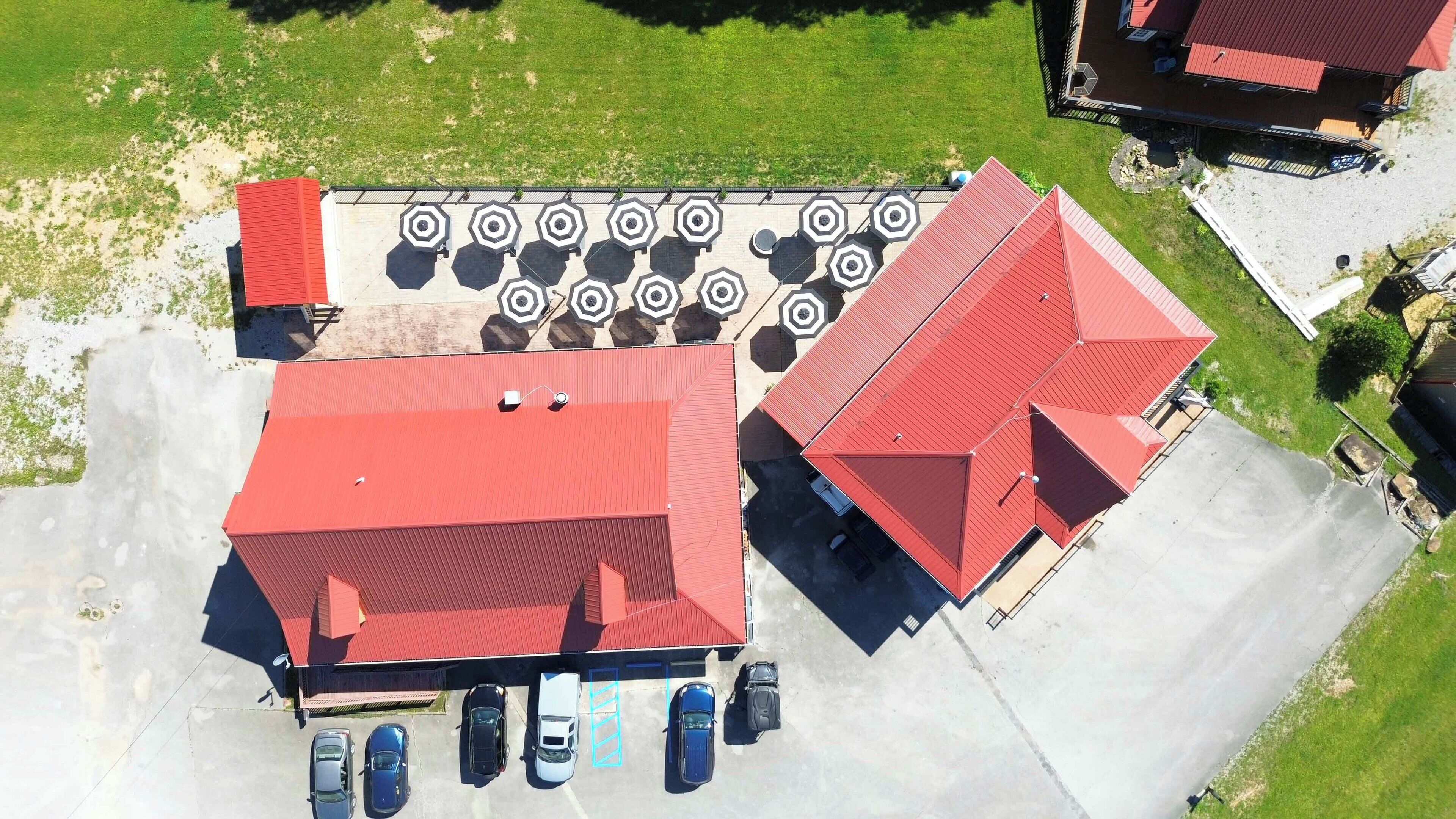 An aerial view of a parking lot with several cars, a building with a red roof, and a grassy area.