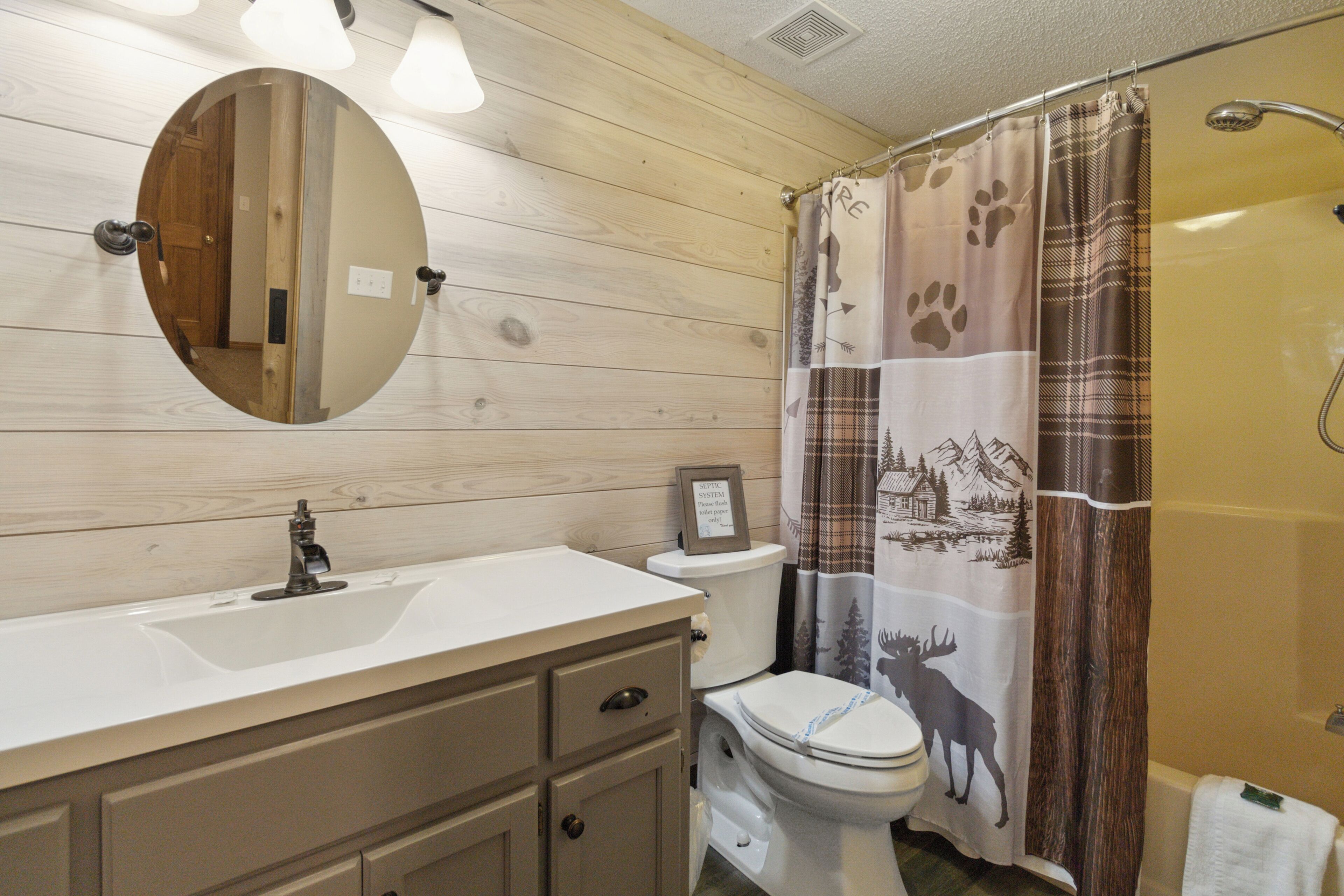 A bathroom with a wooden vanity, a round mirror, a toilet, and a shower curtain with animal prints.