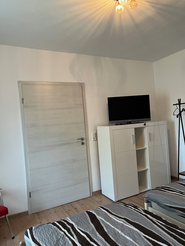 A bedroom with a bed, a wardrobe, a television on top, and a door.