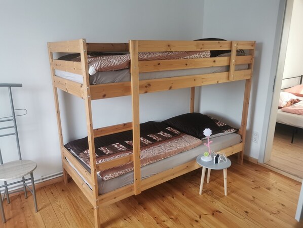 A bunk bed with a metal ladder, a small round table with a power outlet, and a chair.