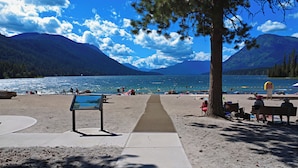 A beach with a clear view of a lake, mountains in the background, and a pathway leading to the water.
