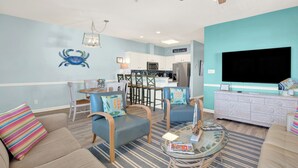 Ein Wohnzimmer mit einer Couch, zwei Sesseln, einem Couchtisch, einem Fernseher und einer Küche im Hintergrund.