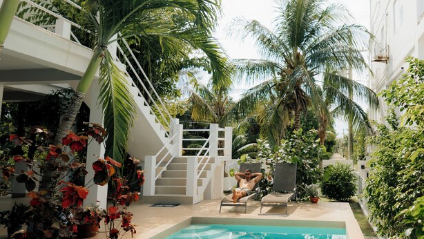 Ein Swimmingpool mit einer Treppe, die zu einem Balkon führt, umgeben von Palmen und Pflanzen.