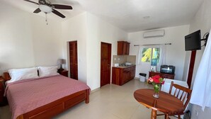 Ein Schlafzimmer mit einem Bett, einem Esstisch mit Stühlen, einer Küchenzeile und einem Deckenventilator.