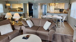 Un salon moderne avec un canapé marron, une table basse et un coin repas comprenant une table et des chaises blanches.