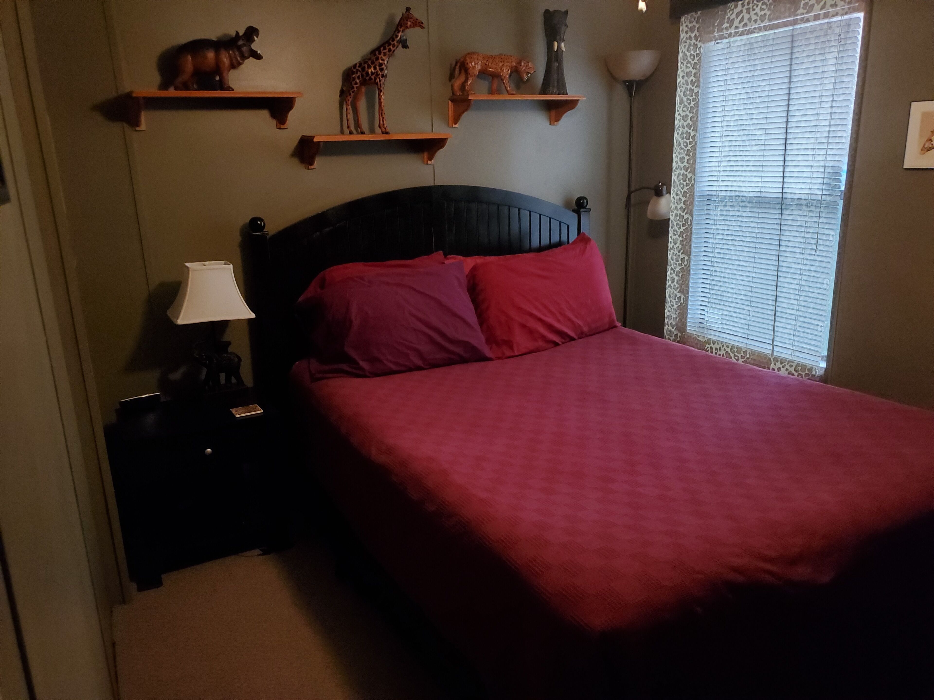 Un dormitorio con una cama, una mesita de noche, una lámpara y estantes en la pared con figuritas de animales.