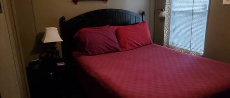 Un dormitorio con una cama, una mesita de noche, una lámpara y estantes en la pared con figuritas de animales.