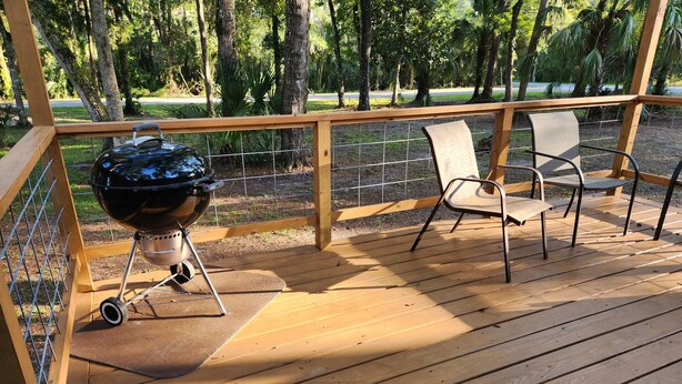 Una terraza de madera con una parrilla y dos sillas de metal.